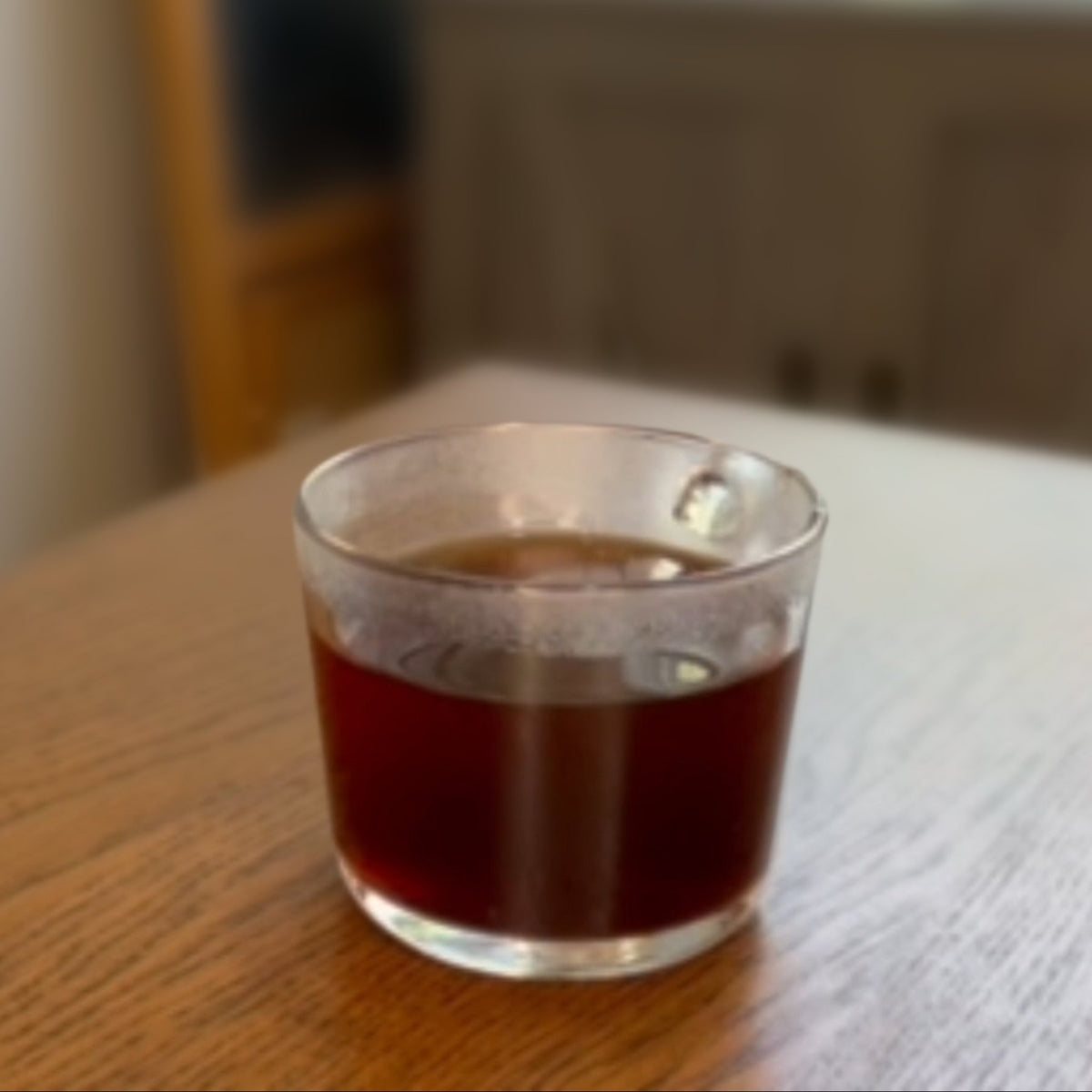 A glass cup of black filter coffee on a wooden table